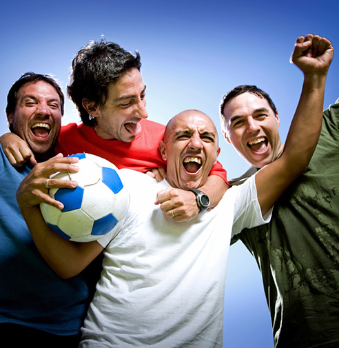 Four happy & raucous male adults, one of them holding a soccer ball
