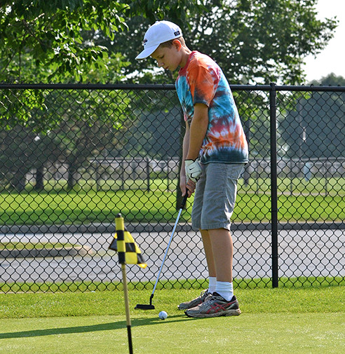Boy concentrating on putting ball into hole at putting green at The Golf Center at SportsOhio