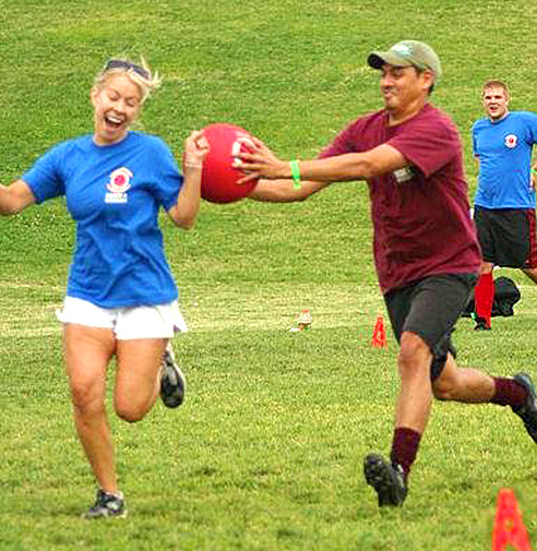 Woman being tagged out by adult male during an outdoor game of Kickball