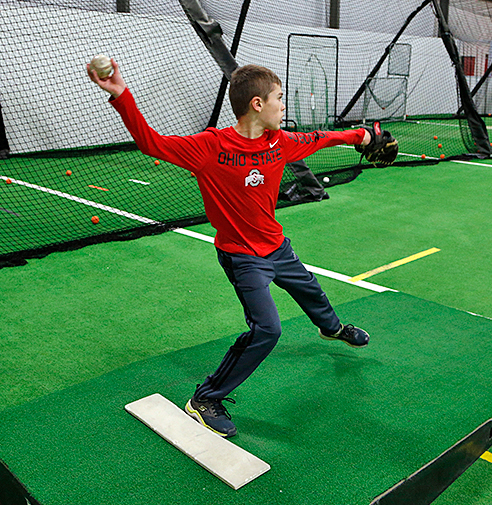 Teen baseball player pitching on an indoor pitching mound